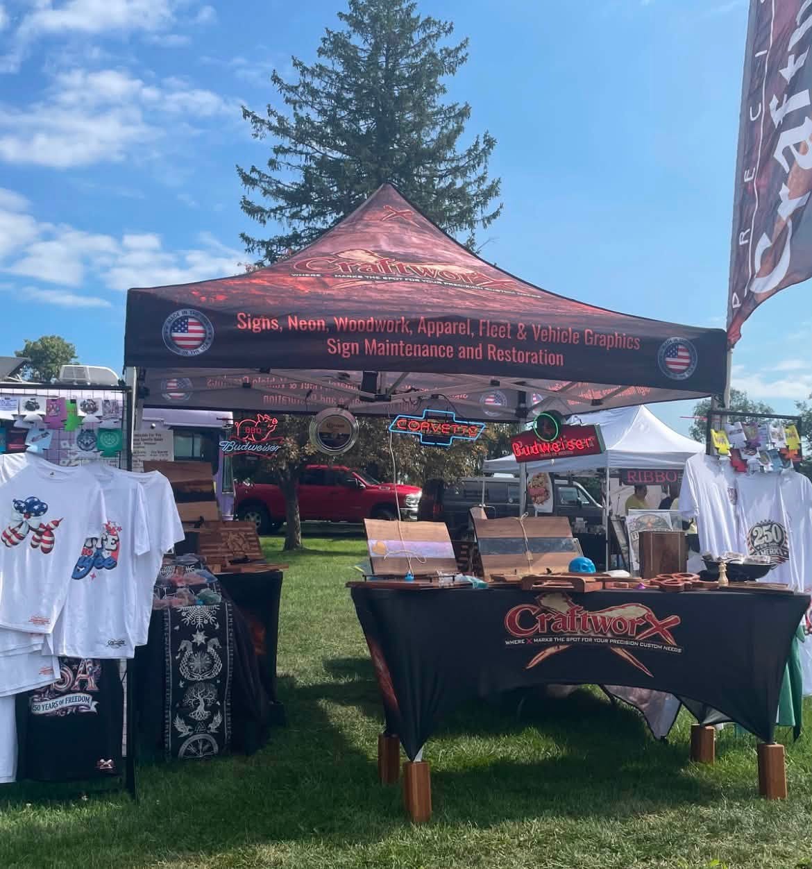 CraftworX fair booth with tent, apparel, wood boards, and neon